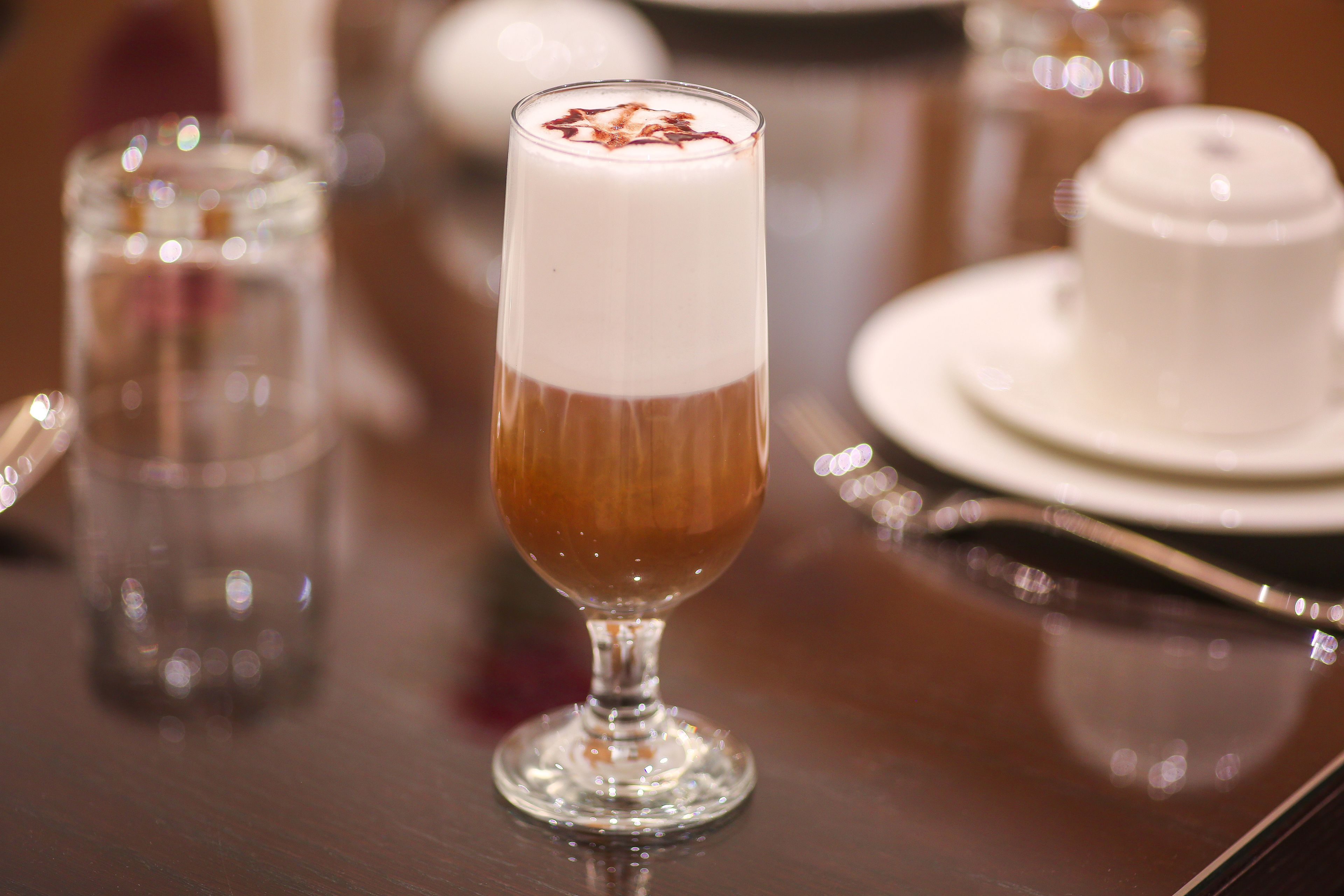Un vaso alto con una bebida en capas, un vaso pequeño y una taza blanca sobre una mesa de madera.