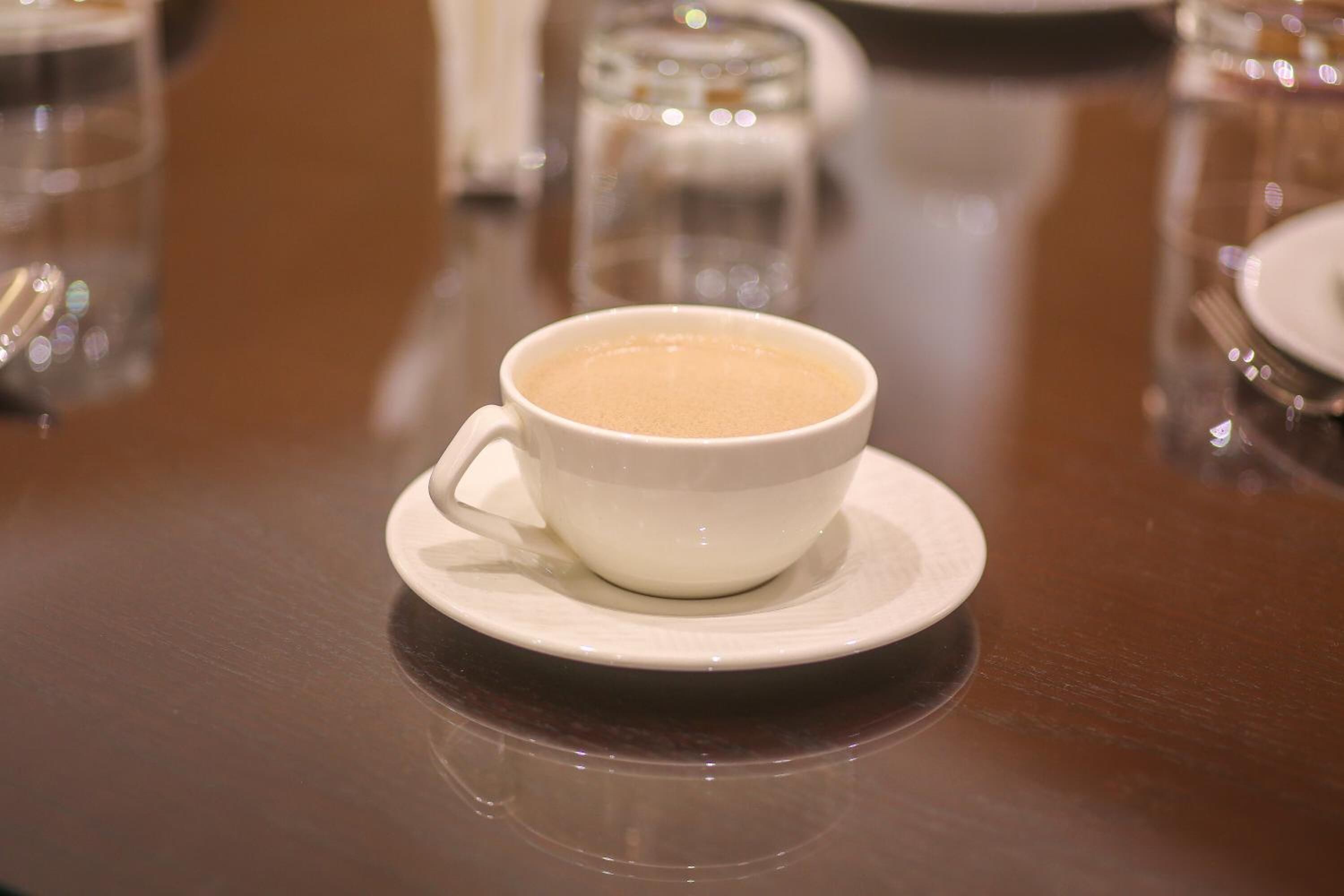 A white cup of coffee on a saucer on a wooden table.