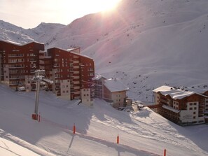Une zone montagneuse enneigée avec des bâtiments, dont un hôtel à plusieurs étages doté de balcons et un télésiège.