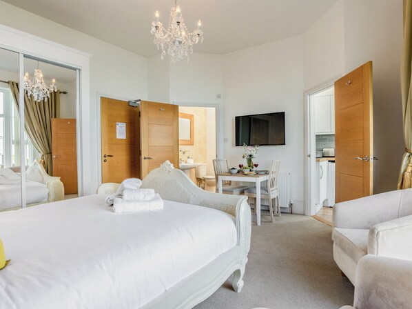 A hotel room with a large bed, a dining table with chairs, a TV mounted on the wall, and a chandelier. - 1 bedroom accommodation in Torquay (Torquay)