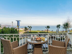 A balcony with wicker furniture, a table with breakfast items, and a view of the sea and mountains. - 1 bedroom accommodation in Torquay (Torquay)