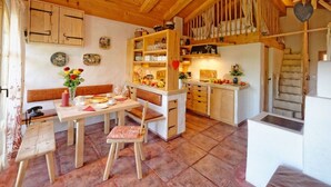 A cozy kitchen with wooden beams, a dining area with a bench, and a staircase leading to an upper level.