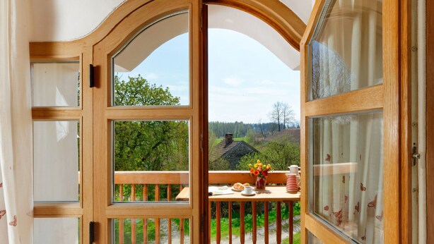 A wooden-framed balcony with a table set for breakfast, overlooking a green landscape.