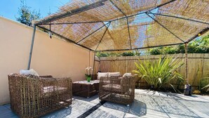 Eine Terrasse im Freien mit Korbmöbeln, einem Tisch und einem Sonnensegel.