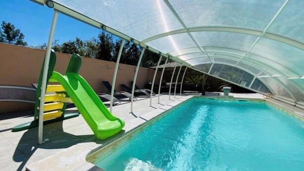 Ein überdachter Pool mit Rutsche, Liegestühlen und einer Pergola.