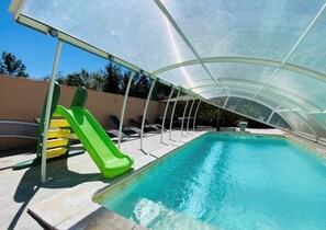 A covered swimming pool with a slide, lounge chairs, and a pergola structure. - Gite du golf with swimming pool (Montauban)