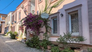 A building with a sign reading "Moshinos Hotel." It features a cobblestone street, potted plants, and a pink facade. - Moshinos Otel (Ayvalik)