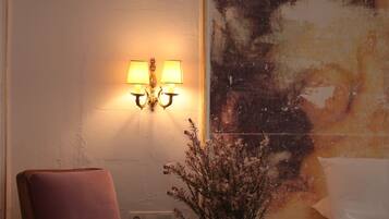 Un dormitorio con cama, una silla, un jarrón con flores y un cuadro en la pared.