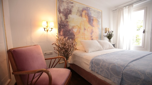A bedroom with a bed, a chair, a painting, and a vase with flowers. - Moshinos Otel (Ayvalik)