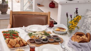 A table set with various dishes, including salads, bread, and condiments, in a well-lit dining area. - Moshinos Otel (Ayvalik)