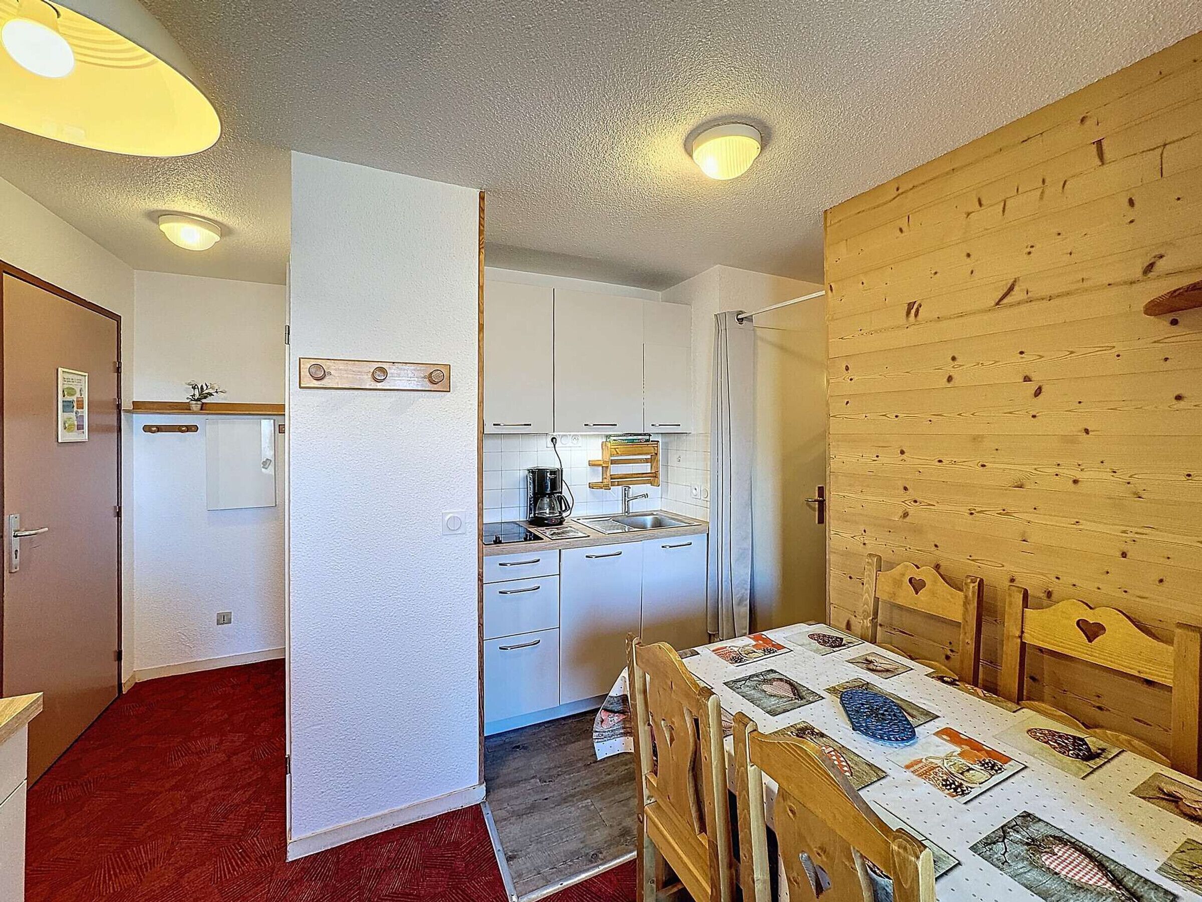 Eine kleine Küche mit weißen Schränken, einer Kaffeemaschine und einem Holztisch mit gesteppter Tischdecke.