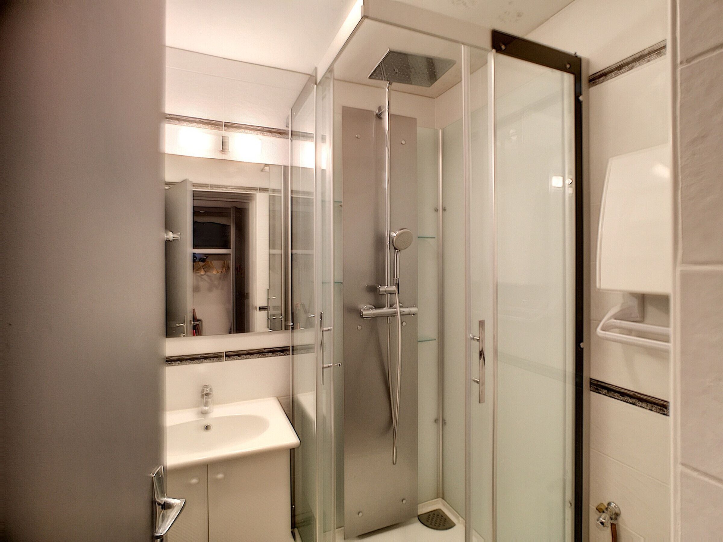 A modern bathroom with a glass-enclosed shower, a sink, and a mirror.