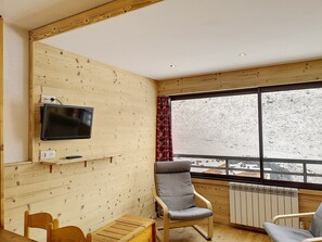 A cozy room with a wooden interior, a television mounted on the wall, a window with a view of a snowy landscape, and a chair.