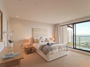 A bedroom with a large bed, bedside tables, a nightstand, a potted plant, and a view of the sea through a balcony. - 3 bedroom accommodation in Westward Ho! (Westward Ho!)