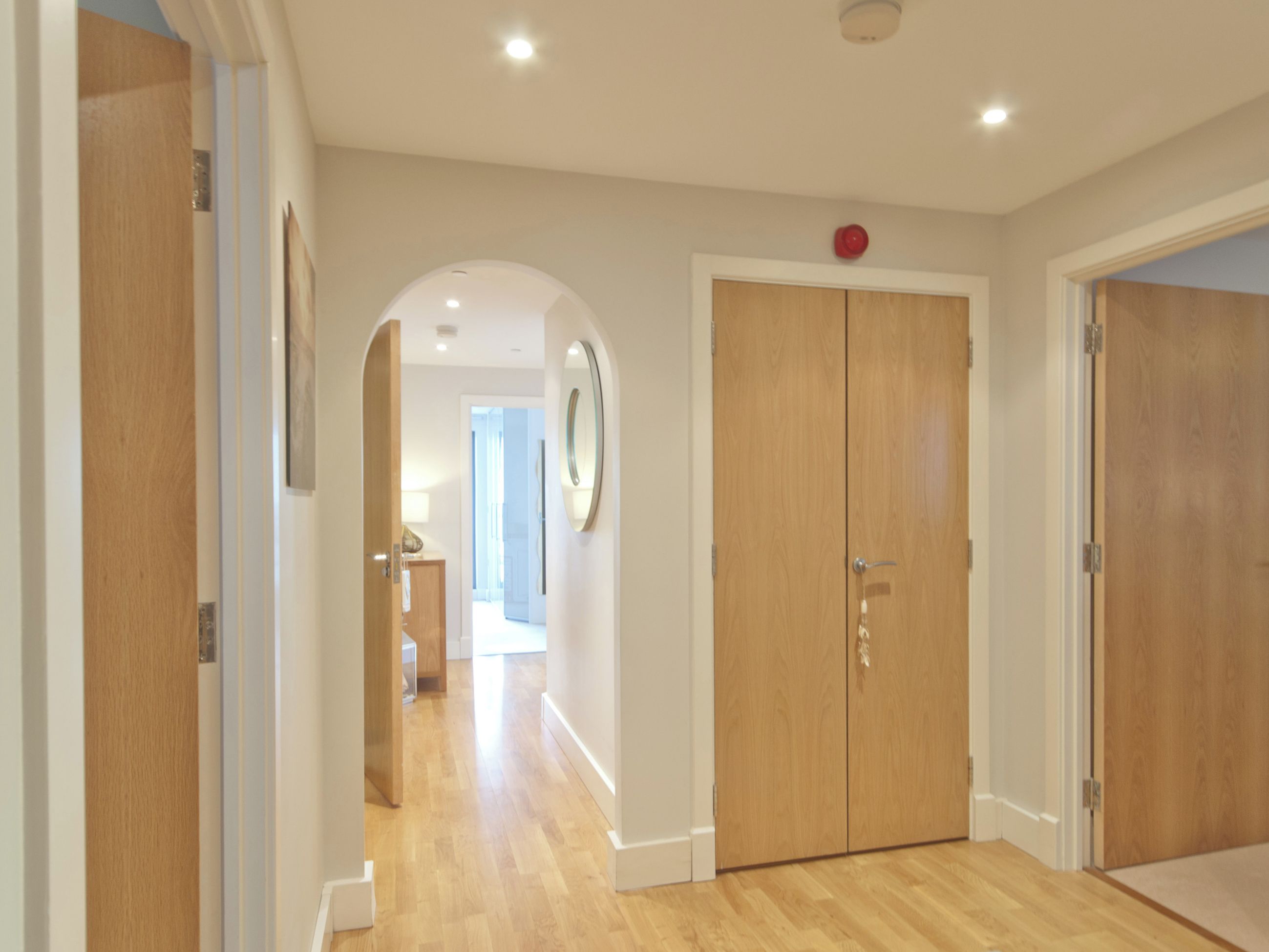 A hallway with wooden flooring, a double door, and a mirror on the wall.