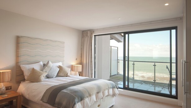 Een slaapkamer met een groot bed, een nachtkastje, een lamp en uitzicht op de oceaan door een schuifdeur.