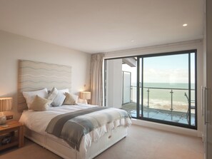 A bedroom with a large bed, a nightstand, a lamp, and a view of the ocean through a sliding glass door. - 3 bedroom accommodation in Westward Ho! (Westward Ho!)
