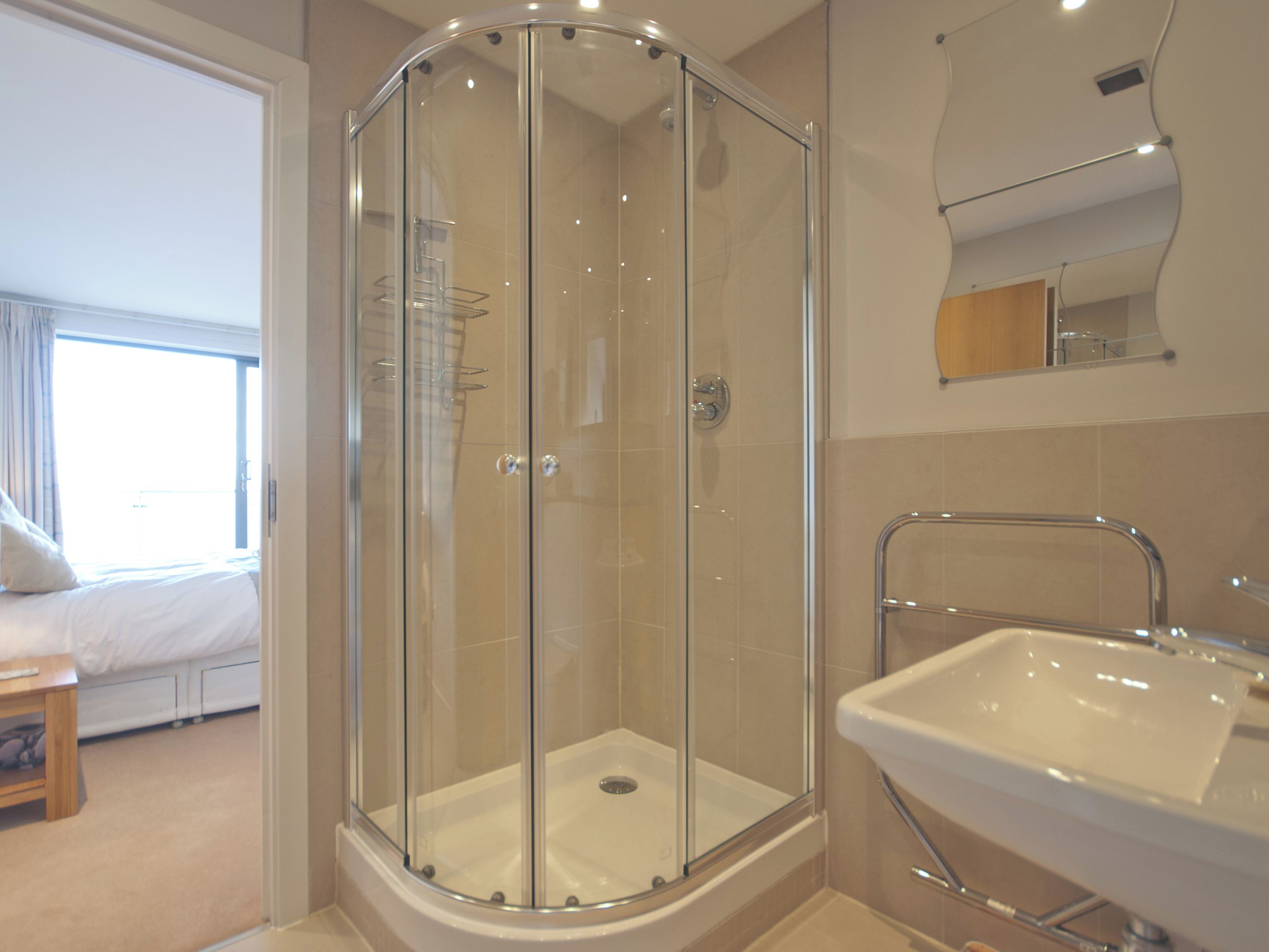 Un baño moderno con ducha de vidrio, lavamanos y espejo.