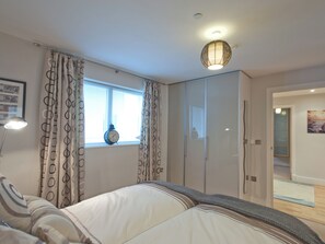 Ein Schlafzimmer mit Bett, Vorhängen, einem Fenster, einer Uhr, einem Kleiderschrank und einer Tür zu einem anderen Raum.