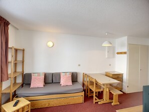 Ein kompakter Raum mit einer Schlafcouch, einem kleinen Tisch, einer Bank und einem Holzregal.