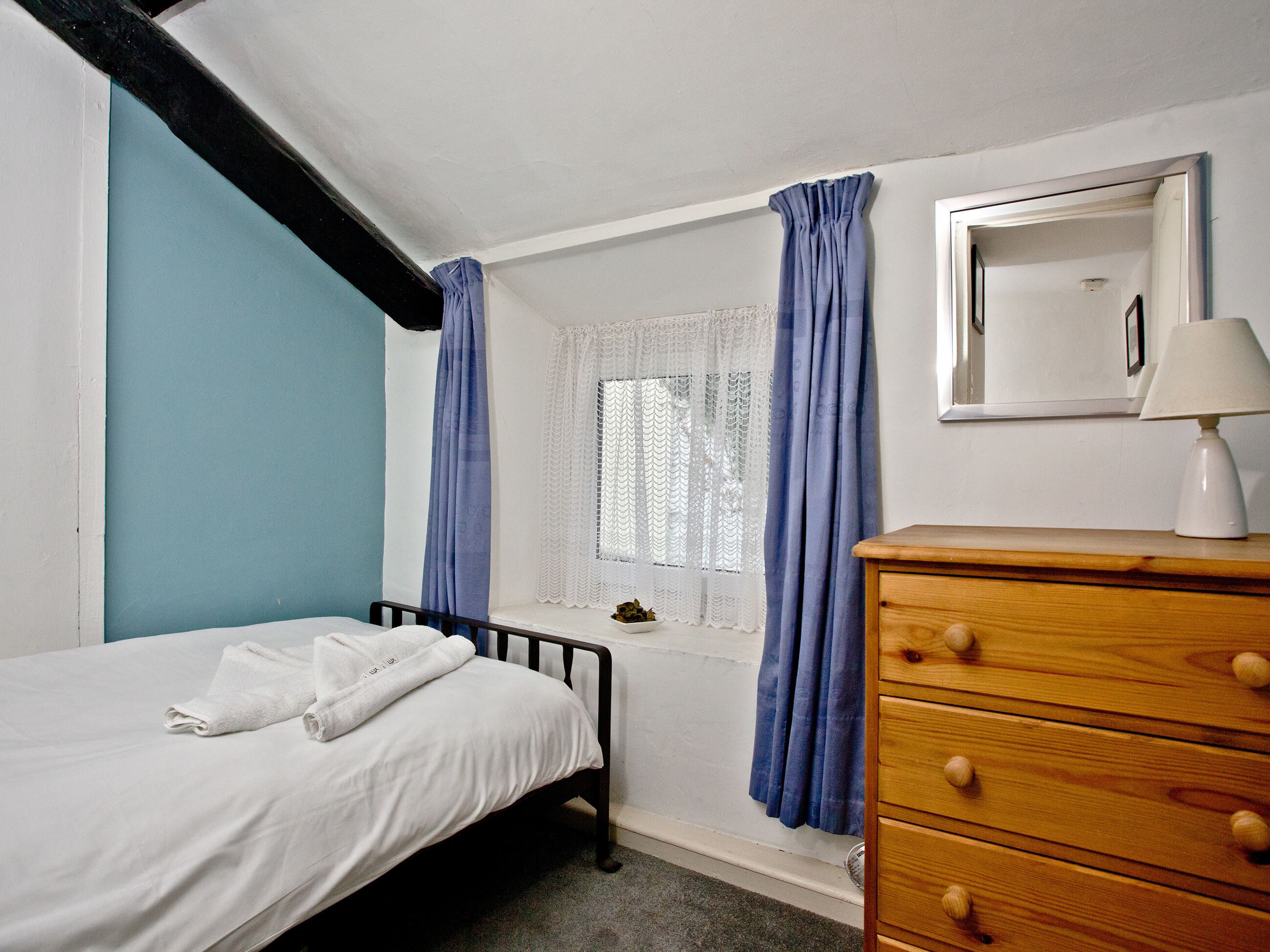 Une chambre à coucher avec un lit, une commode, une fenêtre ornée de rideaux en dentelle et un miroir.
