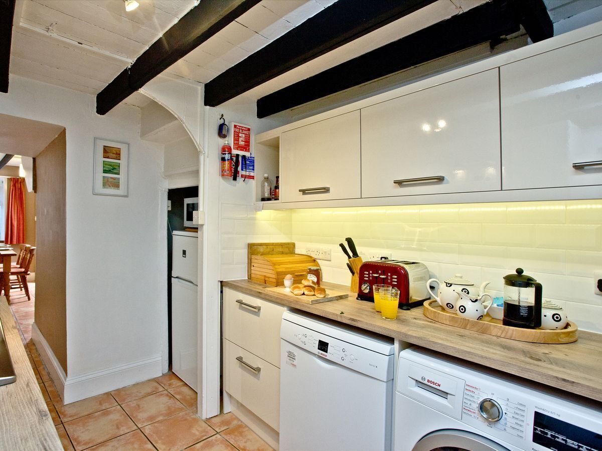 Una cocina compacta con armarios blancos, lavavajillas Bosch y encimera de madera con utensilios de cocina.