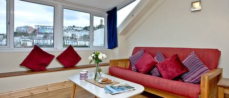 A living room with a red sofa, a white coffee table, and a view of a coastal town through large windows.