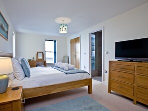 A modern bedroom with a wooden bed, a flat-screen TV, a bedside table with a lamp, and a large window.