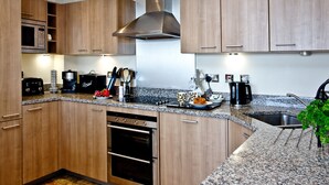 Une cuisine moderne avec des meubles en bois, des appareils électroménagers en acier inoxydable, des plans de travail en granit et un four encastré.