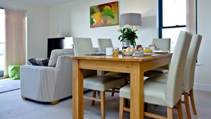 Un coin repas avec une table en bois, quatre chaises, un vase de fleurs et un tableau accroché au mur.