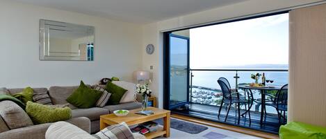 Un salon avec un canapé, une table basse et une vue sur la mer, visible à travers une grande fenêtre.