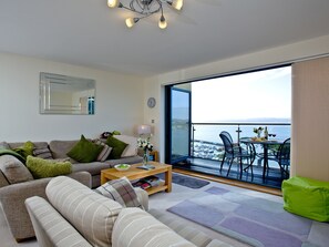 Una sala de estar con sofá, mesa de centro y vista al mar a través de un amplio ventanal.