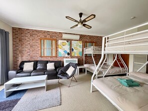 A room with a brick wall, a black leather sofa, a white desk, a bunk bed, and a ceiling fan. - Sunryes Beach House @the Heart of Rye Beach & Shops: Longer Stay Welcome (Rye)