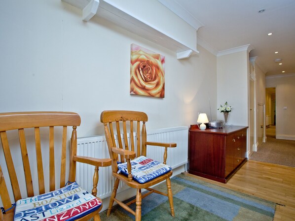 Une pièce avec une chaise en bois, un radiateur, une lampe et un tableau accroché au mur.