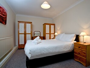 A neatly made bed with white linens, a wooden nightstand with a lamp, a wooden wardrobe, and a wall-mounted mirror.