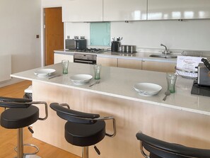 Uma cozinha moderna com uma ilha central, banquetas, forno embutido e cafeteira.