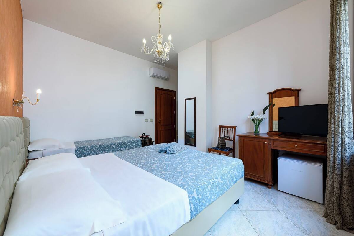 A hotel room with a bed, a desk with a television, a chair, and a mirror.