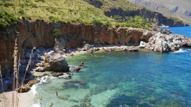 A coastal area with clear water, rocky shore, and greenery. - Araba Fenice (San Vito Lo Capo)