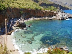 A coastal area with clear water, rocky shore, and greenery. - Araba Fenice (San Vito Lo Capo)