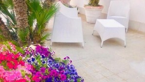 A patio area with white chairs and a variety of colorful flowers. - Araba Fenice (San Vito Lo Capo)