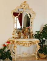 Una consola blanca ornamentada con detalles dorados, un espejo con marco dorado y varios jarrones decorativos.