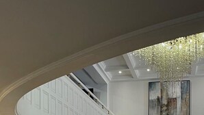 Un hall d’entrée spacieux, doté d’un plafond haut, d’un magnifique lustre et d’un grand tableau abstrait.