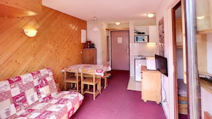 A compact room with a wooden wall, a sofa, a small dining table, and a kitchenette area. - 2-room apartment, 4 pers, ski-in/ski-out, wifi, pets allowed (Les Menuires)