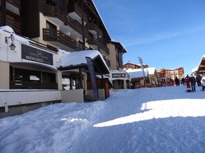 Une rue enneigée bordée d’immeubles, dont un restaurant appelé « Menus » et une station de ski appelée « Skiset ».