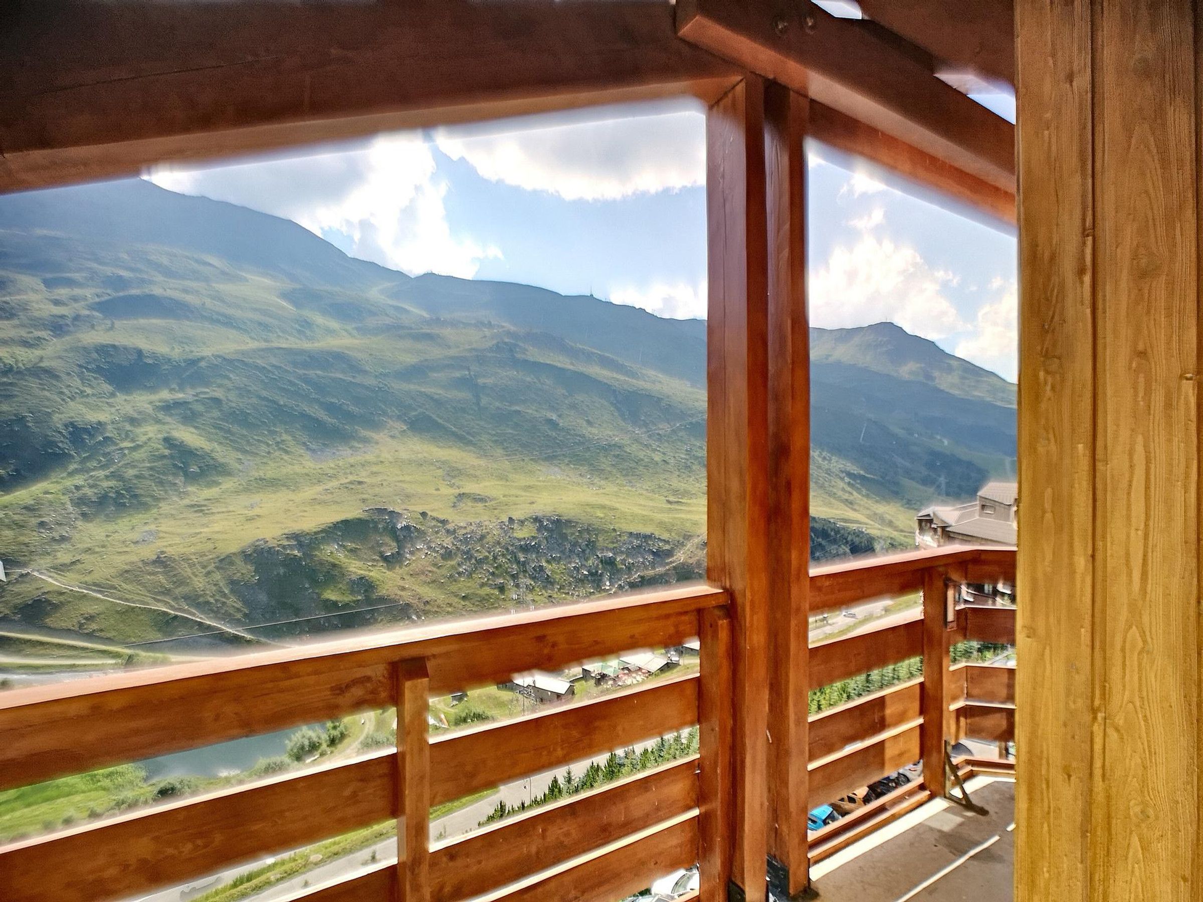 A wooden balcony with a view of green mountains and a valley.