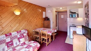 A cozy room with a wooden wall, a sofa, a small table, and a kitchenette. - 2-room apartment, 4 pers, ski-in/ski-out, wifi, pets allowed (Les Menuires)