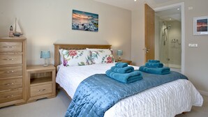 Une chambre à coucher comprenant un lit, une commode en bois, une table de chevet, une cabine de douche en verre et un tableau accroché au mur.
