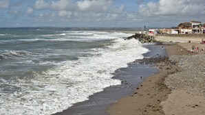 Une plage avec des vagues, une côte rocheuse et des bâtiments en arrière-plan.