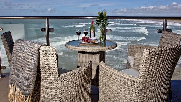 Une table ronde entourée de chaises en osier, sur un balcon donnant sur la mer.