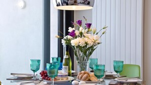 Une table ronde en verre, avec une bouteille de vin, un vase de fleurs et une assiette de pain et de raisins.